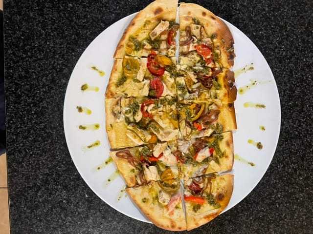A sliced datil flatbread from The Press, topped with grilled chicken, roasted peppers, tomatoes and a pesto drizzle