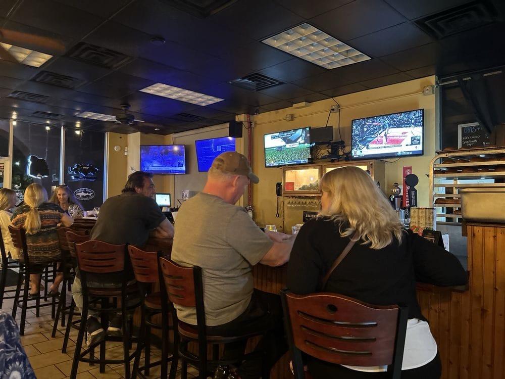 Guests seated at the wooden bar at The Press in St. Augustine, with games on the TVs overhead